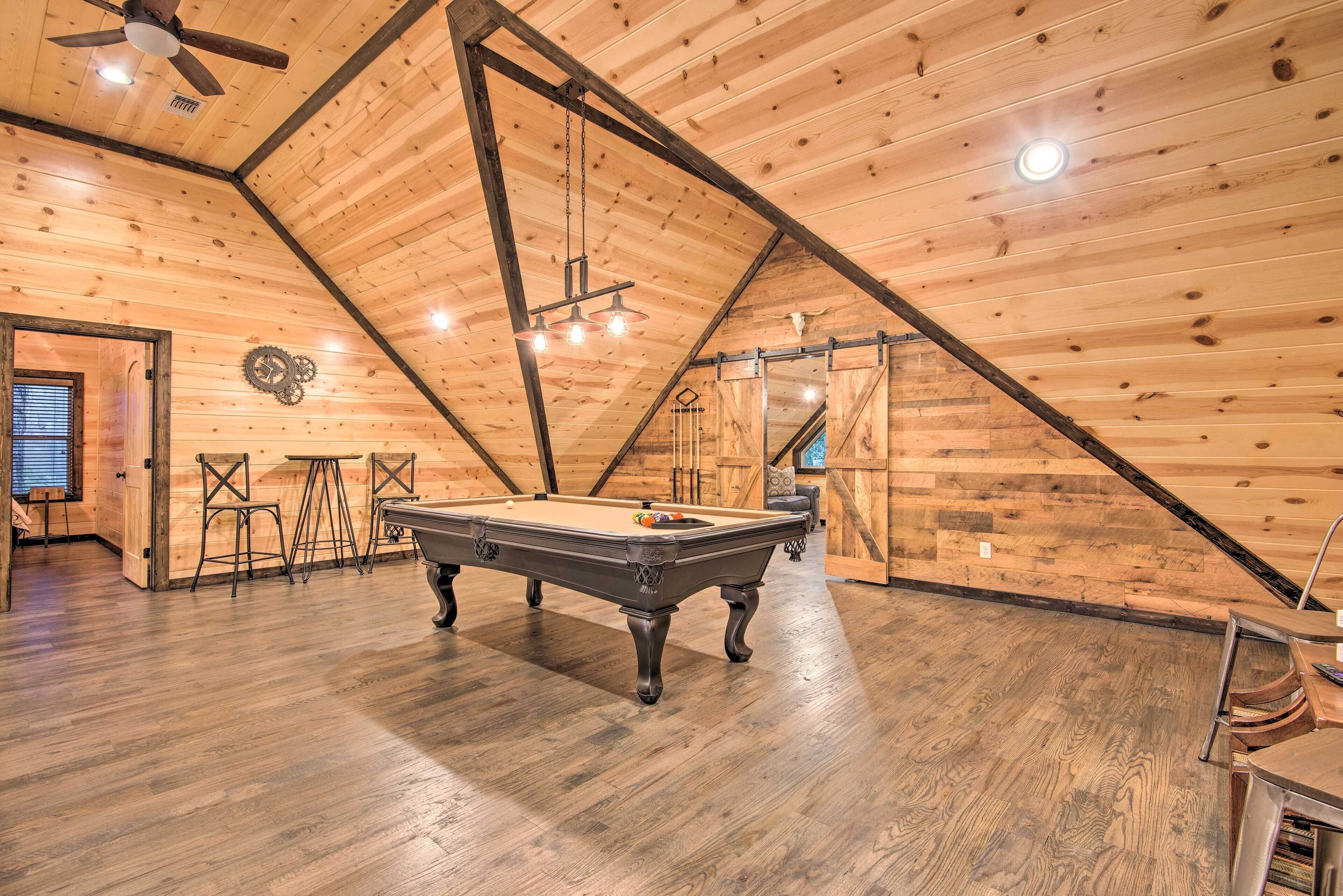 Una habitación amplia con mesa de billar, paredes de madera y techo inclinado.