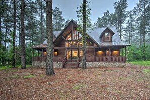 A log cabin with a stone foundation, wooden exterior, and a porch with railings. - Large Upscale Cabin: Hot Tub, Fire Pit, Pool Table (Broken Bow)