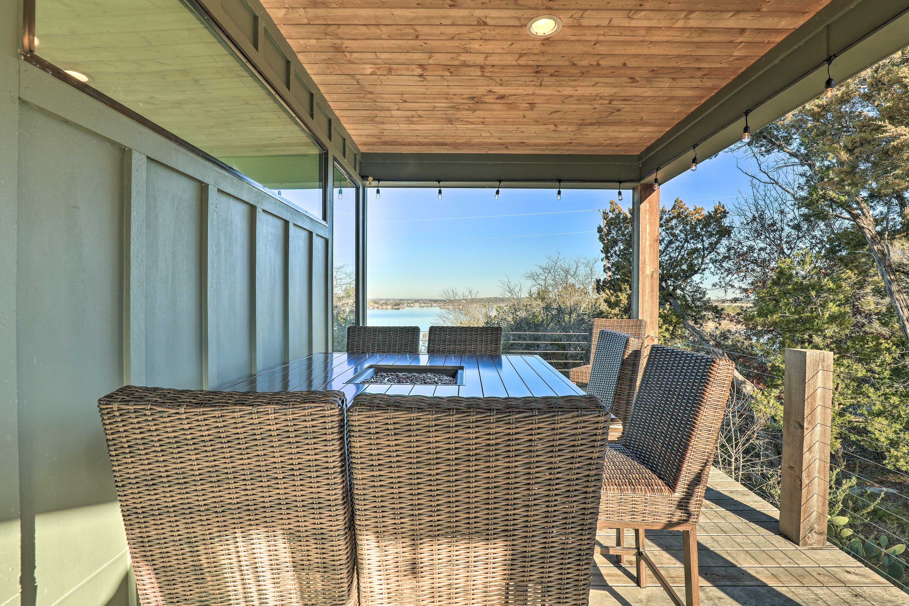 An outdoor patio with a glass table and wicker chairs, overlooking a scenic landscape.