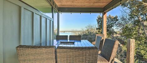An outdoor patio with a glass table and wicker chairs, overlooking a scenic landscape.