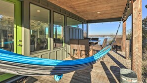Eine Holzterrasse mit einer Hängematte, Korbmöbeln und Blick auf das Wasser.