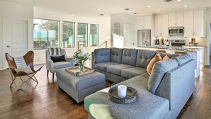 Ein geräumiges Wohnzimmer mit einer Eckcouch, einem Couchtisch und einem Essbereich. Im Hintergrund ist eine Küche zu sehen.