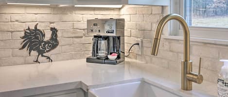 A kitchen with white cabinets, a coffee maker, a brass faucet, and a rooster decoration on the wall.
