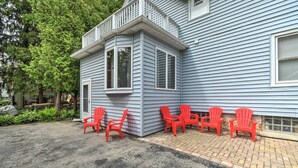Une maison avec une baie vitrée d’angle et une terrasse en briques avec des chaises rouges.