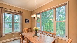 A dining room with a wooden table, chairs, a chandelier, and large windows with curtains.