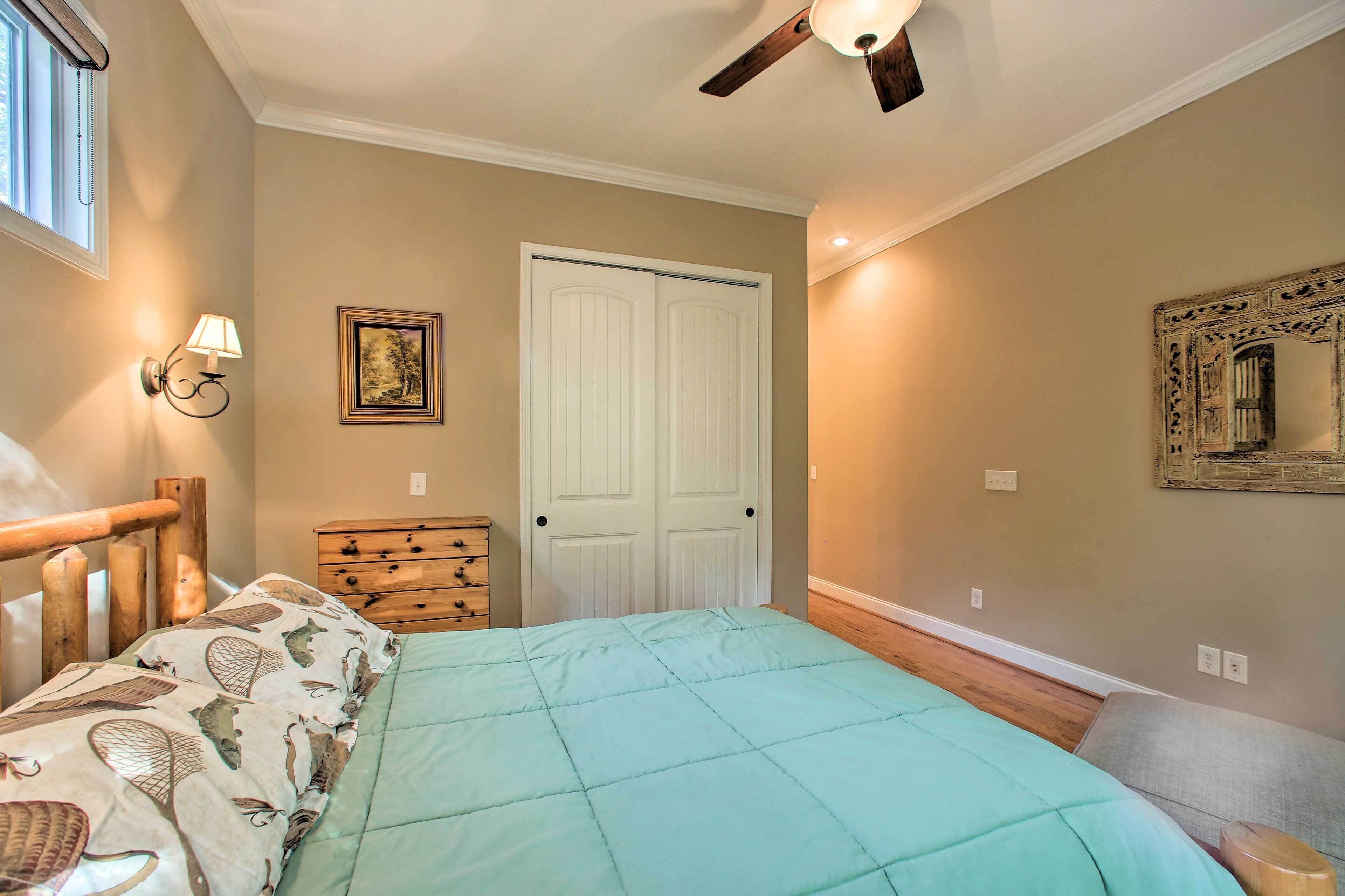 A bedroom with a bed, a wooden dresser, a white door, a ceiling fan, and a wall-mounted lamp.