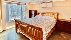 A bedroom with a wooden bed, a dresser, a nightstand, and a window with a view of trees.