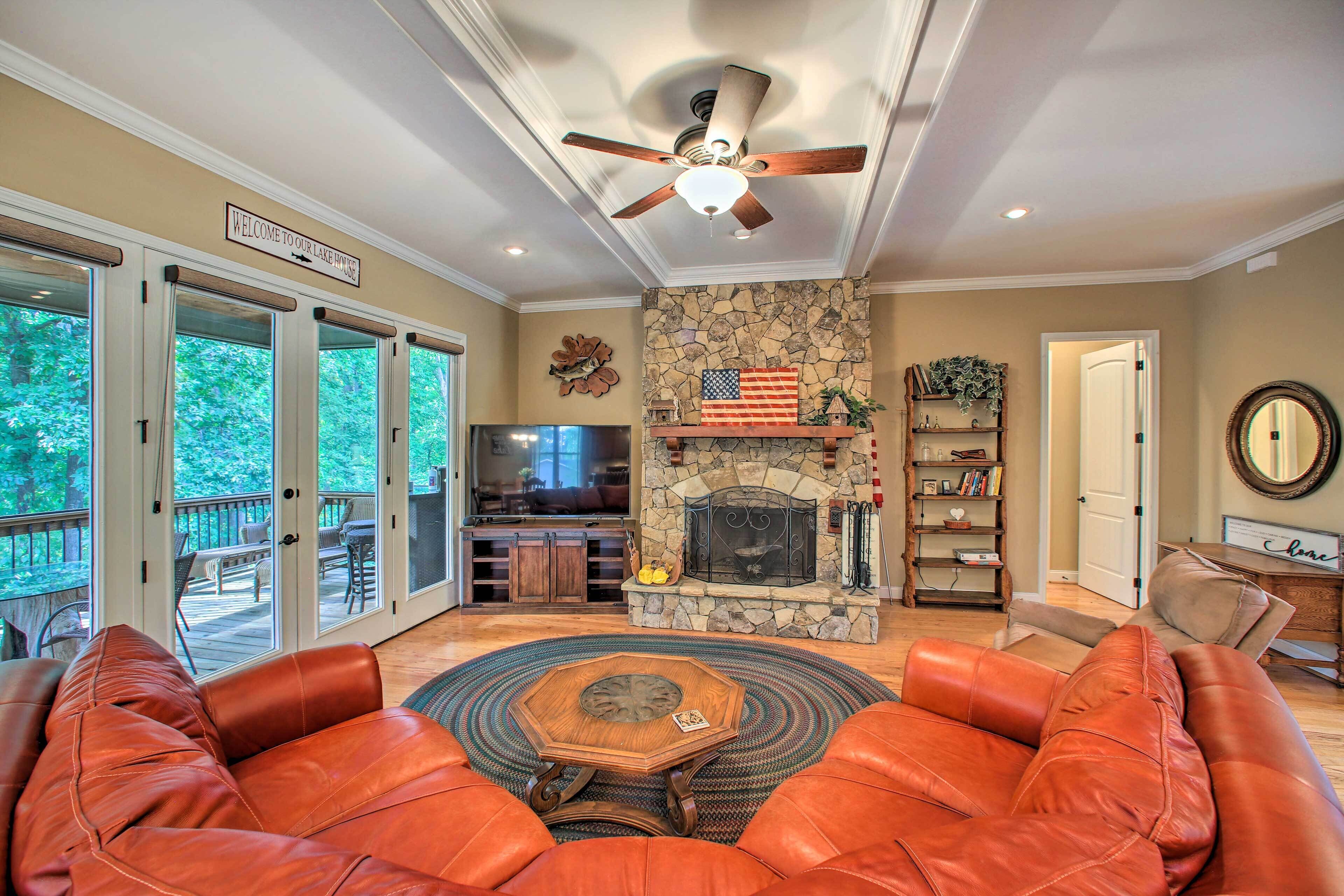 A spacious living room with leather sofas, a stone fireplace, and a ceiling fan.