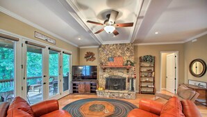A spacious living room with leather sofas, a stone fireplace, and a ceiling fan.