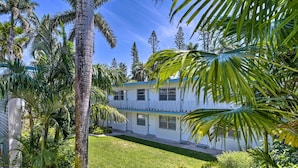 A two-story building with a white exterior and blue trim, surrounded by lush greenery and palm trees. - Luxe Naples Escape: Walk to Beach & Downtown! (Naples)