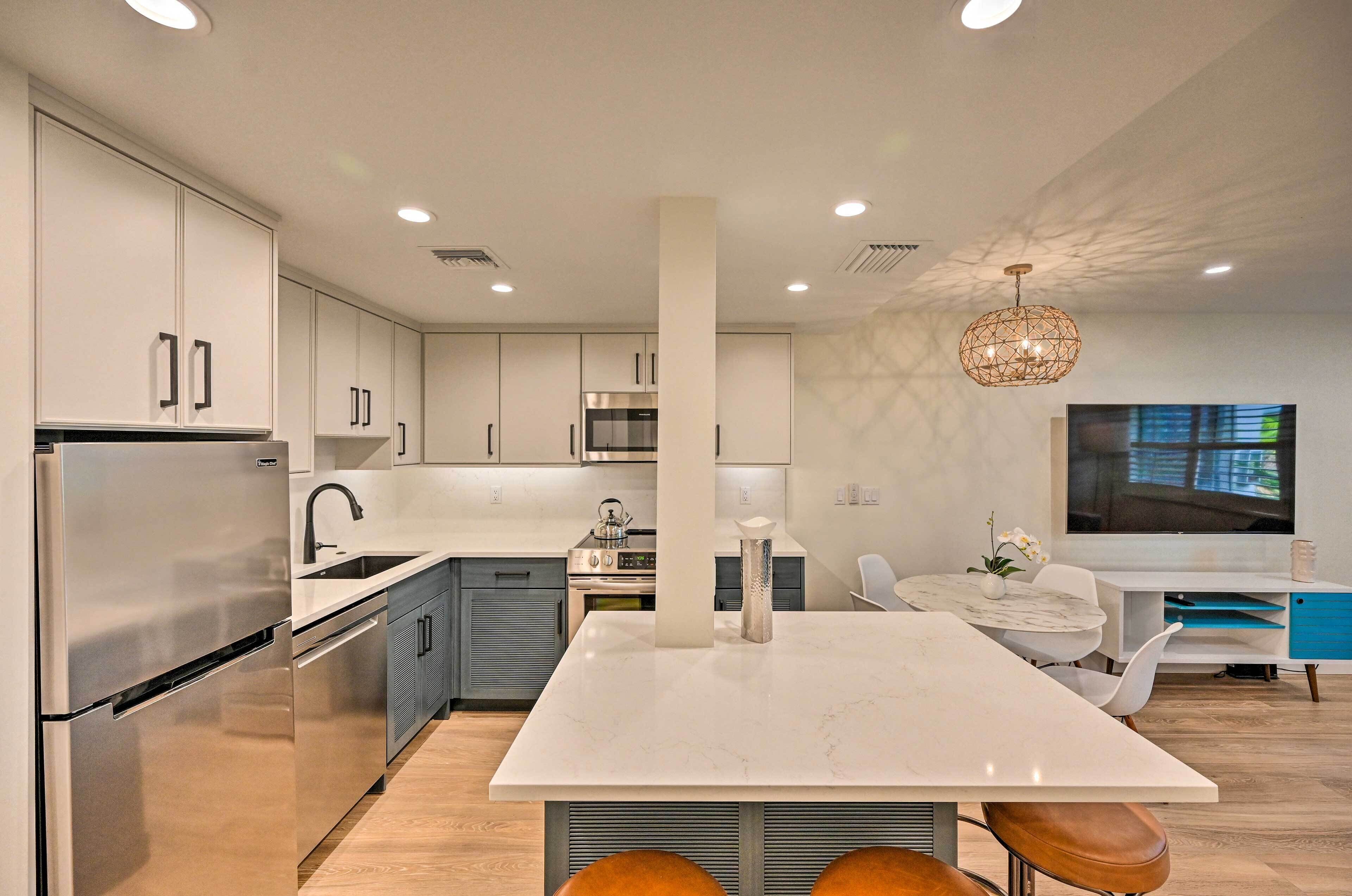 A modern kitchen with stainless steel appliances, a central island, and a dining area with a TV and seating.