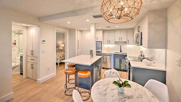 A modern kitchen with white cabinets, a marble island, and a unique geometric pendant light. - Luxe Naples Escape: Walk to Beach & Downtown! (Naples)