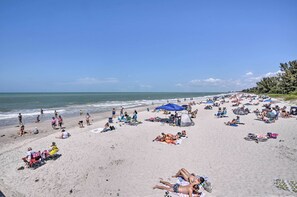 Una playa concurrida, gente tomando el sol, sombrillas y sillas de playa.