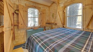 A wooden cabin bedroom with a plaid bedspread, wooden walls, and large windows. - Palmyra Cottage w/ Deck on Whites Pond! (Palmyra)