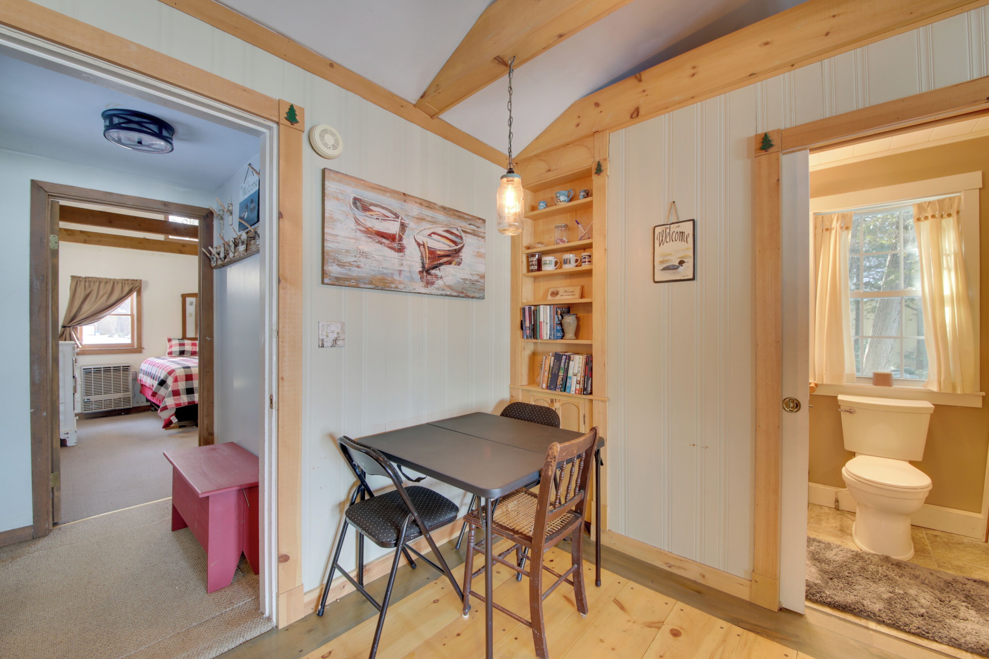 A cozy room with a wooden table and chairs, a bookshelf, a painting, and a window with curtains.