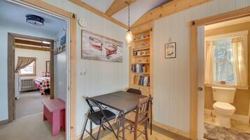 A cozy room with a wooden table and chairs, a bookshelf, a painting, and a window with curtains.