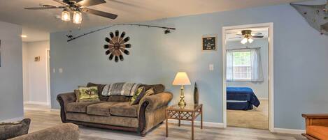 Un salon avec un ventilateur de plafond, un canapé, une lampe et un jeu de fléchettes accroché au mur.