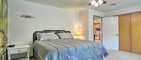 Un dormitorio con cama, mesita de noche, ventilador de techo y una puerta que da a un baño.