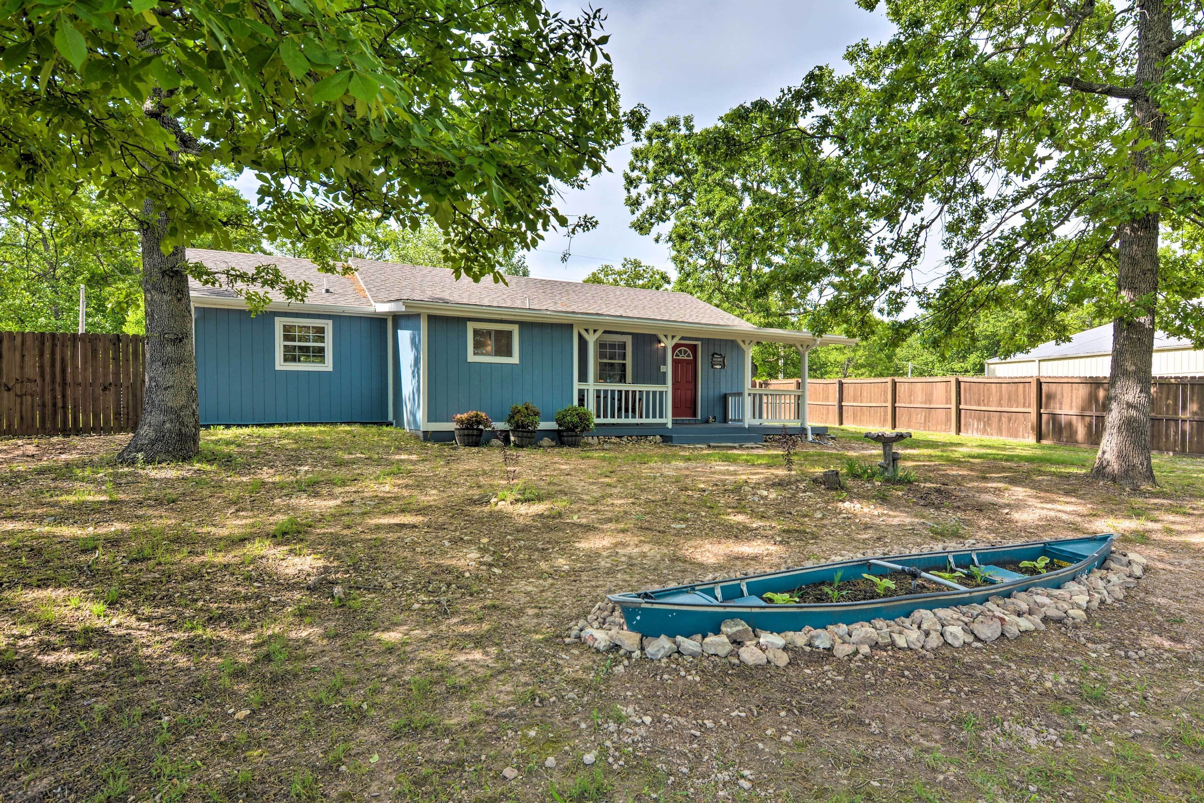 A single-story house with a blue exterior, a front porch, and a small garden area with a boat.