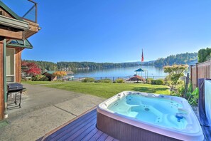 Une terrasse en bois avec un jacuzzi, un barbecue et une vue sur un lac, agrémentée d’un belvédère et d’un mât portant un drapeau.