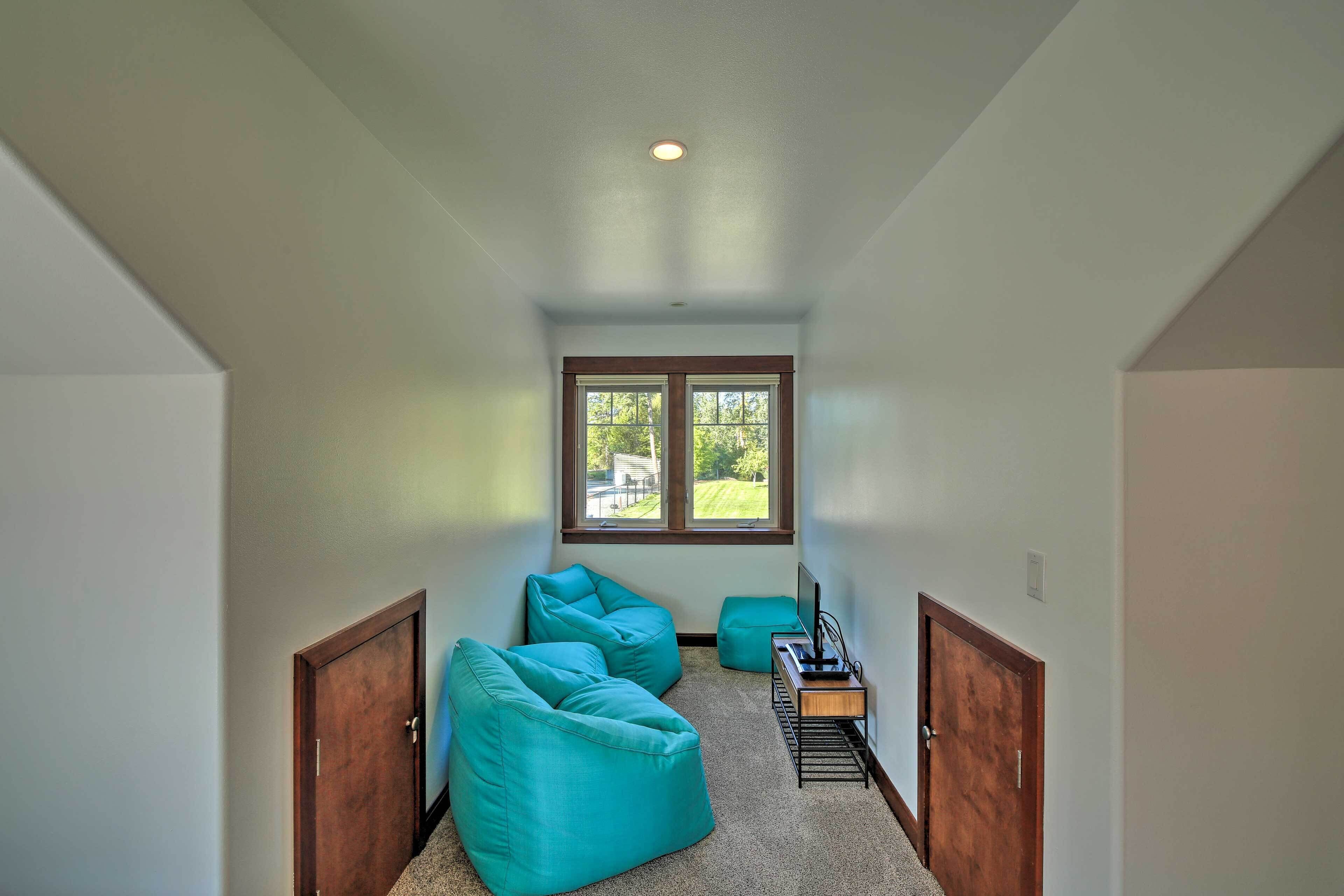 A narrow hallway with teal bean bag chairs, a small table with a laptop, and a window with a view of greenery.