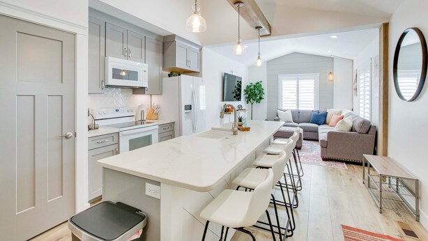 A modern kitchen with a central island, bar stools, and a dining area with a sofa and table. - Logan Area Home Near Willard Bay State Park! (Brigham City)