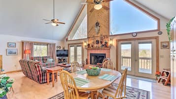 A spacious living room with a high ceiling, a fireplace, and a large dining table with chairs.