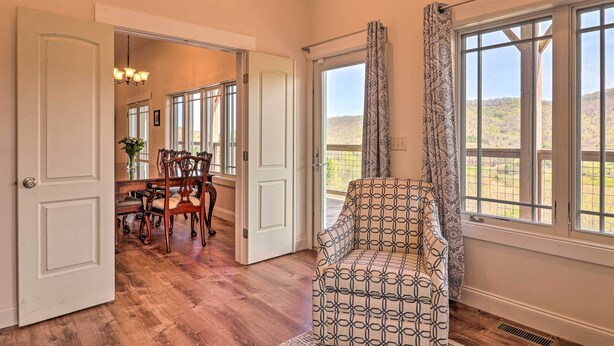 A spacious room with a dining area, a patterned armchair, and large windows with a view of the outdoors. - Mountain Refuge w/ View, 12 Mi to Asheville! (Candler)
