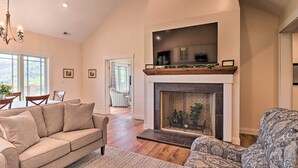 A spacious living room with a fireplace, a sofa, a patterned armchair, and a dining area with chairs and a table. - Mountain Refuge w/ View, 12 Mi to Asheville! (Candler)