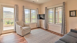 A spacious room with a large window, a ceiling fan, a patterned armchair, a grey sofa, and a flat-screen TV. - Mountain Refuge w/ View, 12 Mi to Asheville! (Candler)