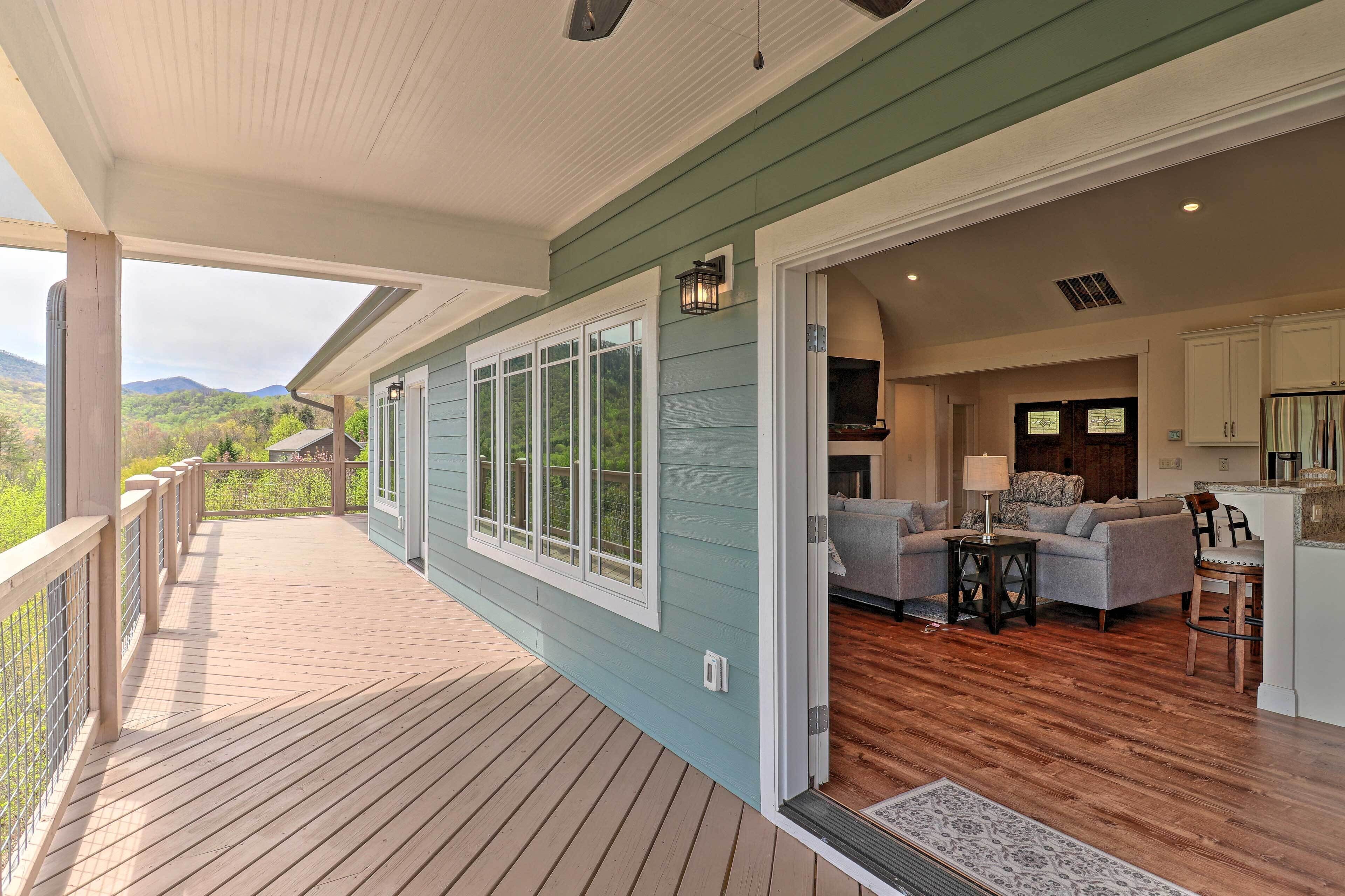 A covered deck with a view of mountains, a living area with a sofa and table, and a kitchen area.