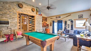 A cozy room with a pool table, a blue sofa, and a stone wall. - Spacious Victorian Home 1/4 Mi to Holiday Valley! (Ellicottville)