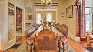 A dining room with a long wooden table, upholstered chairs, a chandelier, and a brick wall. - Spacious Victorian Home 1/4 Mi to Holiday Valley! (Ellicottville)