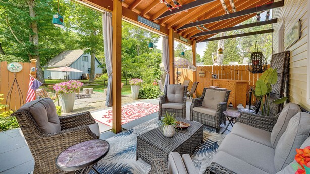 A covered outdoor seating area with wicker furniture, a coffee table, and a view of the backyard. - Spacious Victorian Home 1/4 Mi to Holiday Valley! (Ellicottville)