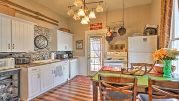 A kitchen with white cabinets, a wooden floor, a dining table with chairs, and a hanging light fixture.