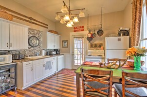 Una cocina con armarios blancos, suelo de madera, una mesa de comedor con sillas y una lámpara colgante.