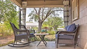 An outdoor patio with wicker furniture, a table, and a view of a house and trees.
