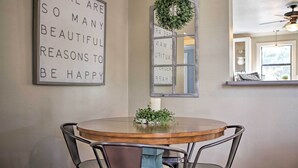 A dining area with a round wooden table, metal chairs, a wall-mounted sign, and a decorative wreath.