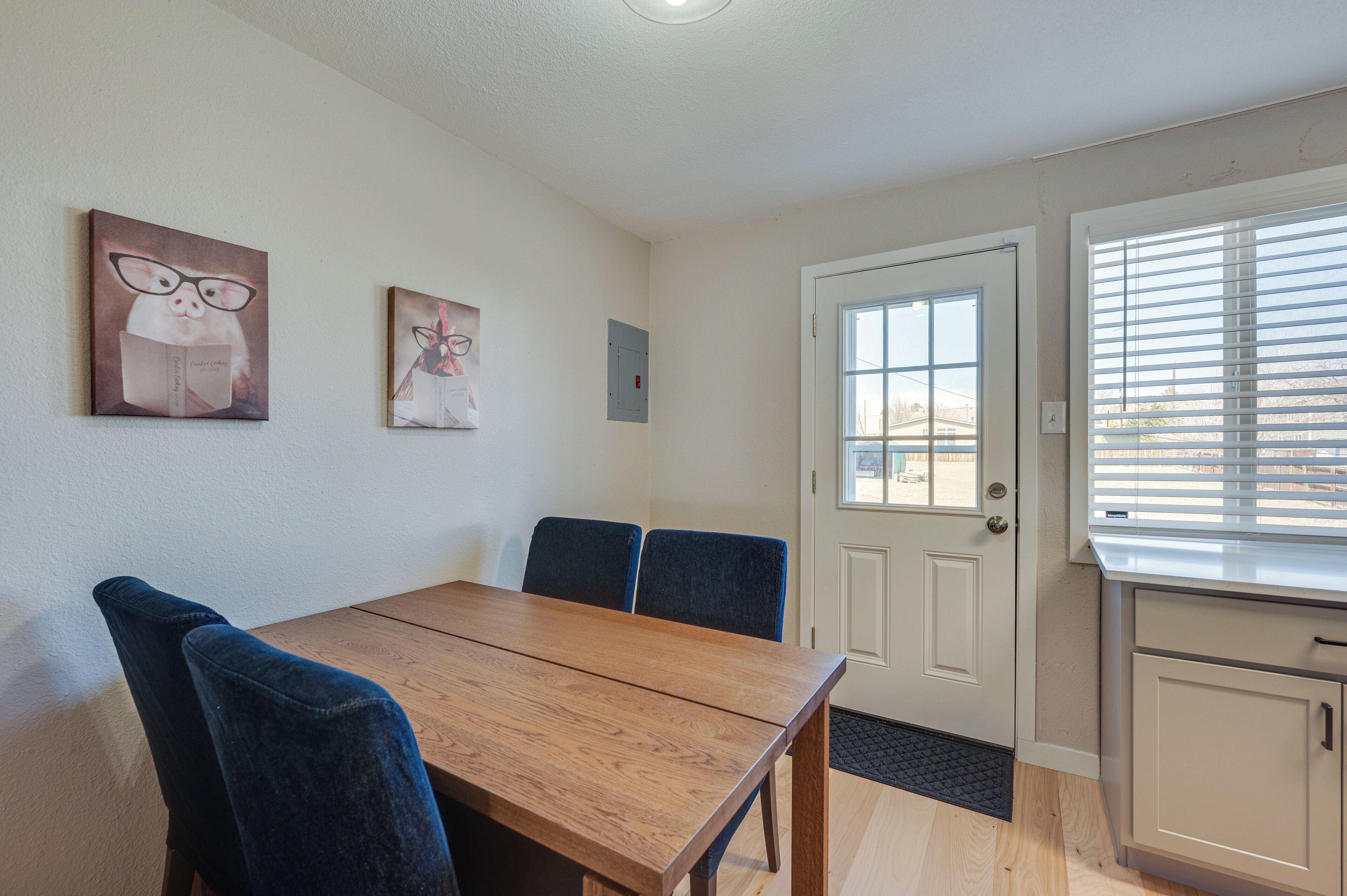 A dining area with a wooden table and blue chairs, a white door, and a window with blinds.