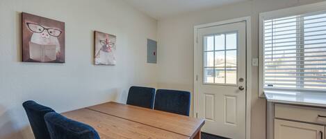 A dining area with a wooden table and blue chairs, a white door, and a window with blinds.