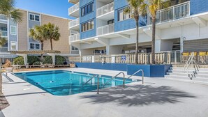 A swimming pool adjacent to a multi-story building with balconies and palm trees.