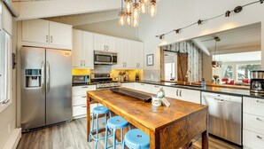 A modern kitchen with white cabinets, stainless steel appliances, a wooden island with stools, and pendant lighting. - Modern Mountain Escape on Golf Course w/ Hot Tub! (Avon)