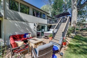 A modern outdoor living area with a red sofa, wicker chairs, a stone fire pit, and a staircase leading to a deck. - Modern Mountain Escape on Golf Course w/ Hot Tub! (Avon)