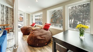 A modern living room with large windows, a dining area, and a seating area with bean bags. - Modern Mountain Escape on Golf Course w/ Hot Tub! (Avon)