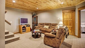 Ein gemütliches Wohnzimmer mit Holzbalkendecke, einem braunen Sofa, einem Fernseher und einem Bücherregal.