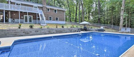 A swimming pool with a wooden deck and a brick house in the background.