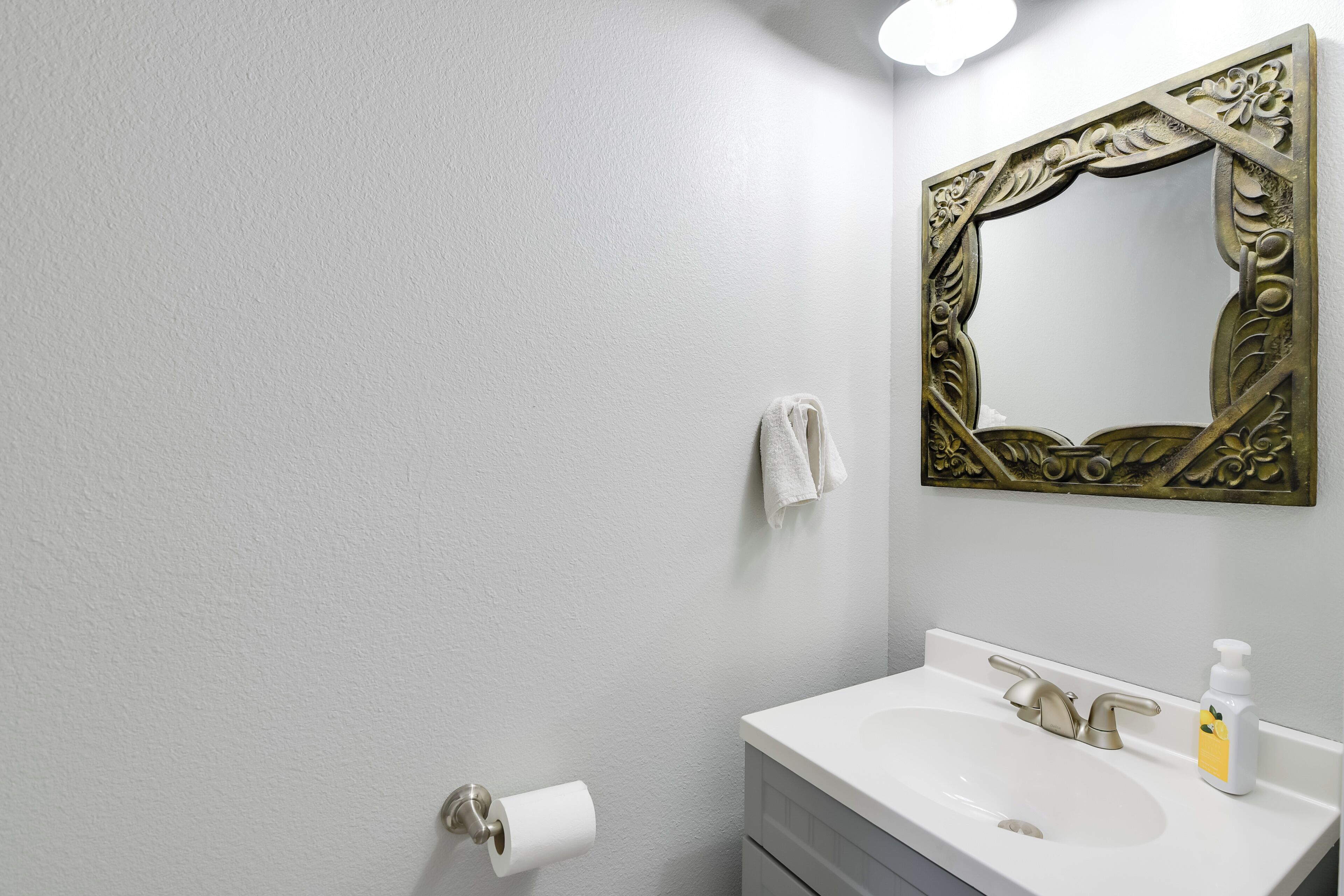 A bathroom with a white sink, a gold-framed mirror, a towel hanging on the wall, and a toilet paper holder.