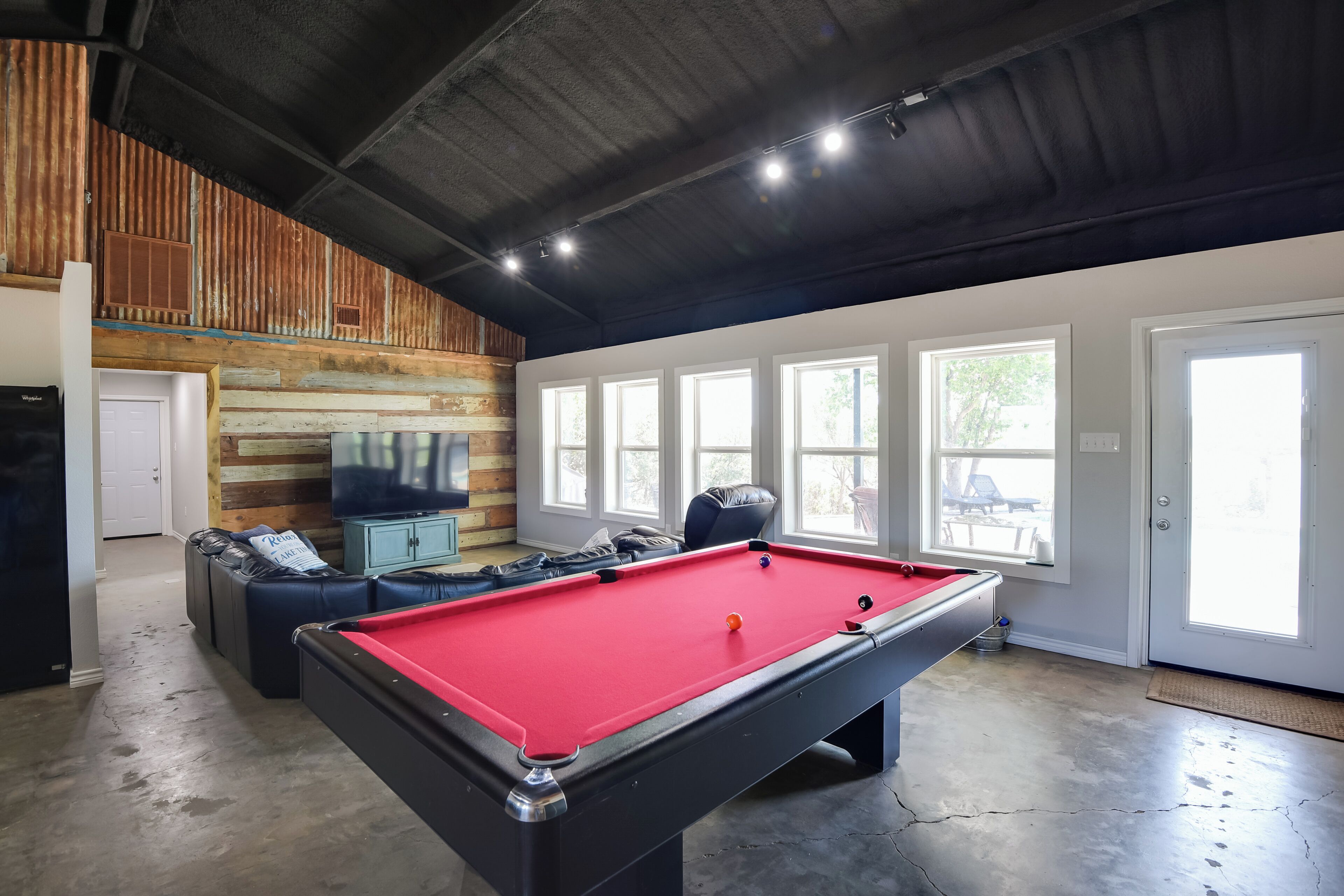 A pool table in a room with a high ceiling, large windows, and a wooden accent wall.