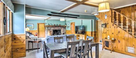 A spacious living area with a wooden dining table and chairs, a fireplace, and a kitchen in the background.