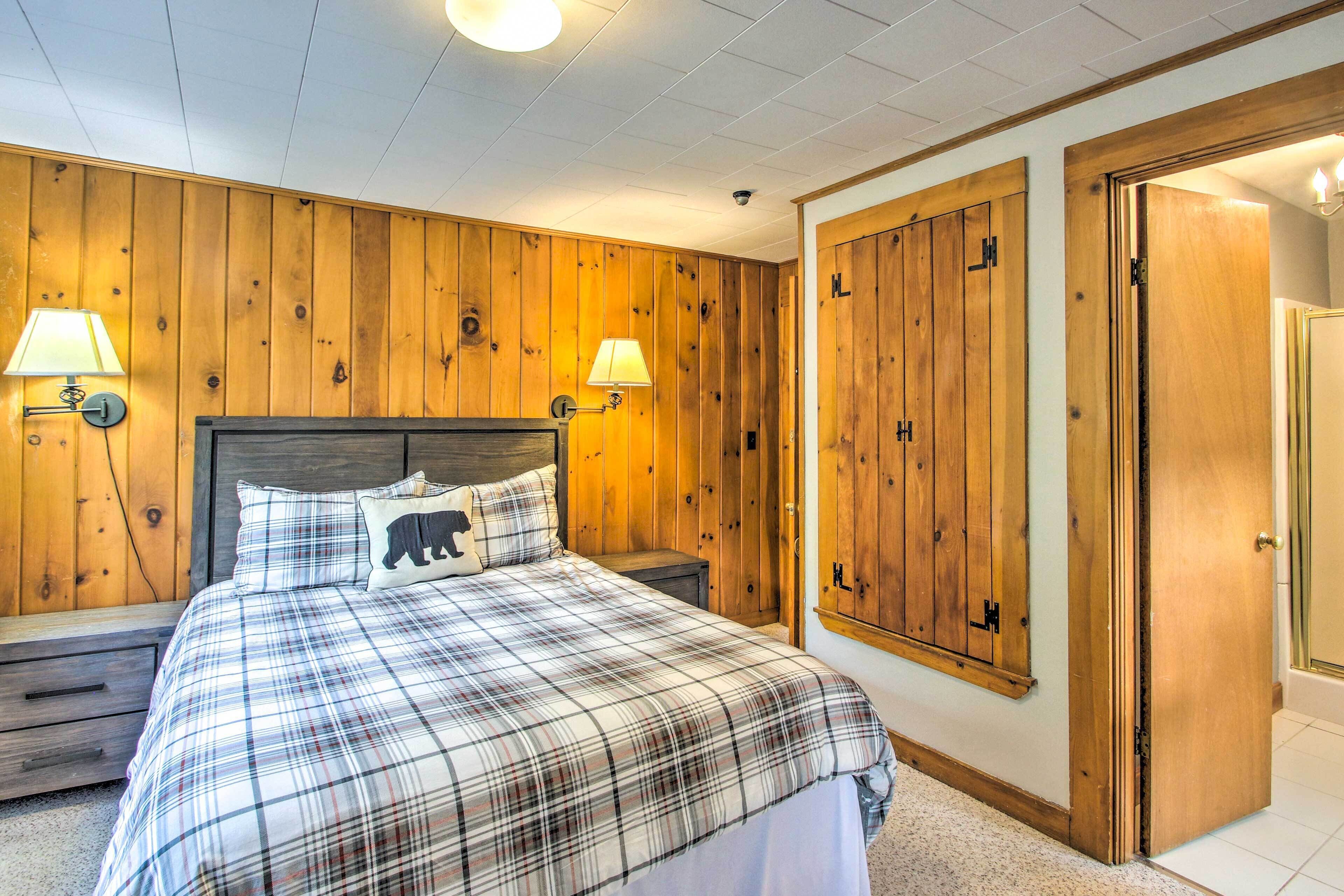 A bedroom with a plaid bedspread, wooden panel walls, two bedside lamps, a nightstand, and a wardrobe with a mirror.